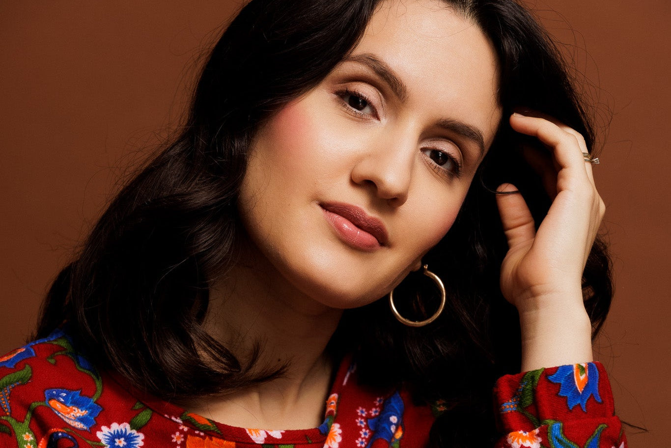 A young woman th wavy brown hair looking into the camera with dreamy eyes and wears a bright red flannel sweatshirt with turkish anatolian floralprint